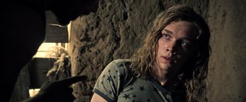 Movie still from “All the Money in the World” (2017), directed by Ridley Scott – A man with long hair is standing in front of a rock wall; Close Up shot, Over the shoulder angle