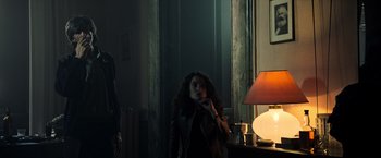 Movie still from “All the Money in the World” (2017), directed by Ridley Scott – A woman standing next to a lamp in a dark room; Medium shot, Low angle