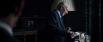 Movie still from “All the Money in the World” (2017), directed by Ridley Scott – An older man in a suit writing on a piece of paper; Medium shot, Low angle