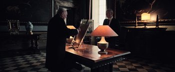 Movie still from “All the Money in the World” (2017), directed by Ridley Scott – Two men are sitting at a table with a lamp; Medium shot, High angle