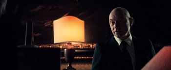Movie still from “All the Money in the World” (2017), directed by Ridley Scott – A man in a suit and tie in front of a lamp; Close Up shot, Low angle