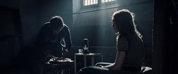 Movie still from “All the Money in the World” (2017), directed by Ridley Scott – Two people sitting in a dark room with a coffee pot on a table; Medium shot, Over the shoulder angle