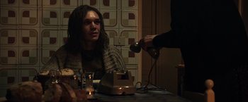 Movie still from “All the Money in the World” (2017), directed by Ridley Scott – A woman sitting at a table with a man pouring water into a cup; Medium shot, Over the shoulder angle