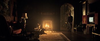 Movie still from “All the Money in the World” (2017), directed by Ridley Scott – A man standing in front of an open fire place; Wide shot, Over the shoulder angle