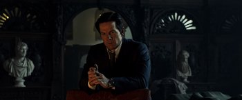 Movie still from “All the Money in the World” (2017), directed by Ridley Scott – A man in a suit and tie holding a cell phone in his hands; Close Up shot, Low angle
