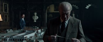 Movie still from “All the Money in the World” (2017), directed by Ridley Scott – An older man in a suit and tie holding a knife; Medium shot, Low angle