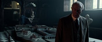 Movie still from “All the Money in the World” (2017), directed by Ridley Scott – A man standing in front of a model of a city; Medium shot, Over the shoulder angle