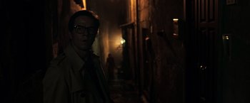 Movie still from “All the Money in the World” (2017), directed by Ridley Scott – A man in a trench coat and glasses in a dark alley; Medium shot, Over the shoulder angle