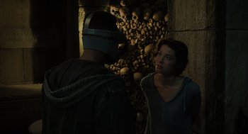 Movie still from “Gemini Man” (2019), directed by Ang Lee – A man and a woman standing in front of a wall of skulls; Close Up shot, Over the shoulder angle