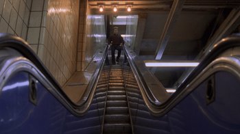 Movie still from “Ghost” (1990), directed by Jerry Zucker – A man riding an escalator down the side of a building; Wide shot, High angle