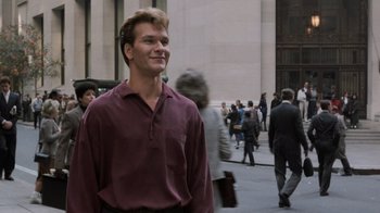 Movie still from “Ghost” (1990), directed by Jerry Zucker – A man in a maroon shirt is smiling for the camera; Medium shot, Low angle