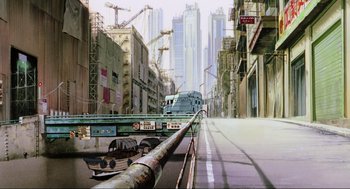 Movie still from “Ghost in the Shell” (1995), directed by Mamoru Oshii – A city street with a train on the side of the road; Extreme Wide shot, Low angle