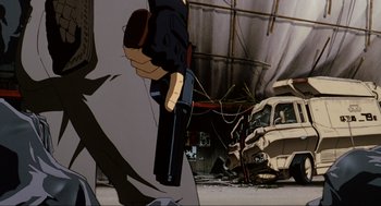 Movie still from “Ghost in the Shell” (1995), directed by Mamoru Oshii – A man holding a gun in a garage with a truck; Wide shot, Low angle