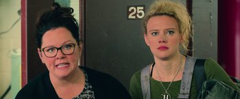 Movie still from “Ghostbusters” (2016), directed by Paul Feig – Two women standing next to each other in front of a wall; Close Up shot, Over the shoulder angle