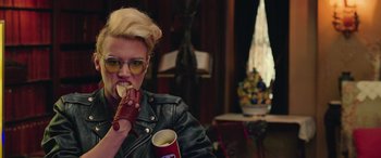 Movie still from “Ghostbusters” (2016), directed by Paul Feig – A woman eating a donut while holding a cup of coffee; Medium shot, Over the shoulder angle
