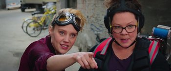 Movie still from “Ghostbusters” (2016), directed by Paul Feig – Two women are posing for a picture while wearing goggles; Close Up shot, Over the shoulder angle