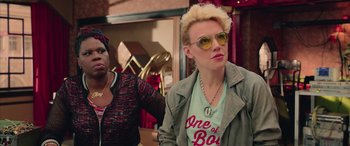 Movie still from “Ghostbusters” (2016), directed by Paul Feig – A woman with blonde hair wearing a green jacket and yellow sunglasses; Close Up shot, Over the shoulder angle
