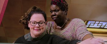 Movie still from “Ghostbusters” (2016), directed by Paul Feig – Two women posing for a picture in a room; Close Up shot, Over the shoulder angle