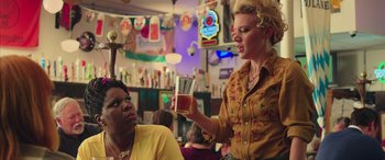 Movie still from “Ghostbusters” (2016), directed by Paul Feig – A woman is serving a drink to another woman; Medium shot, Over the shoulder angle