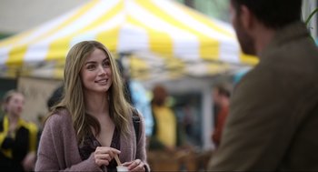 Movie still from “Ghosted” (2023), directed by Dexter Fletcher – A young woman is talking to a man in front of a tent; Medium shot, Over the shoulder angle