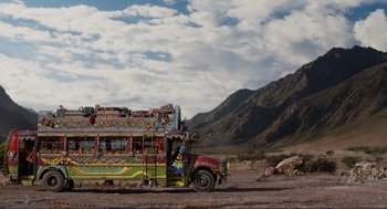 Movie still from “Ghosted” (2023), directed by Dexter Fletcher – A colorful bus parked on the side of a road; Extreme Wide shot, Low angle