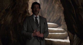 Movie still from “Ghosted” (2023), directed by Dexter Fletcher – A man in a suit and tie standing in front of a stone staircase; Medium shot, Low angle