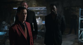 Movie still from “Ghosted” (2023), directed by Dexter Fletcher – A group of men standing next to each other in a dark room; Medium shot, Over the shoulder angle