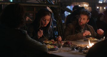Movie still from “Ghosted” (2023), directed by Dexter Fletcher – A group of people sitting at a table eating food; Medium shot, Over the shoulder angle