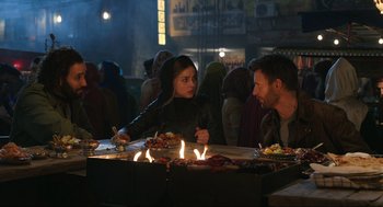 Movie still from “Ghosted” (2023), directed by Dexter Fletcher – A group of people sitting around a fire pit; Medium shot, Over the shoulder angle