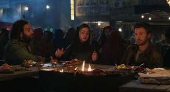 Movie still from “Ghosted” (2023), directed by Dexter Fletcher – A woman is cooking food on an outdoor grill; Medium shot, Over the shoulder angle