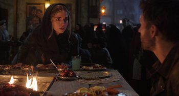 Movie still from “Ghosted” (2023), directed by Dexter Fletcher – A woman sitting at a table with a plate of food in front of her; Medium shot, Over the shoulder angle
