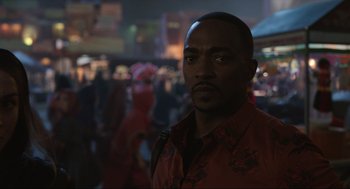Movie still from “Ghosted” (2023), directed by Dexter Fletcher – A man in a red shirt is standing in front of a group of people; Close Up shot, Over the shoulder angle
