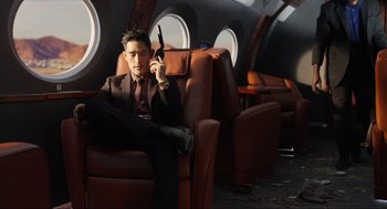 Movie still from “Ghosted” (2023), directed by Dexter Fletcher – A man sitting on a chair holding a pair of scissors in his hand; Medium shot, Low angle