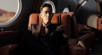 Movie still from “Ghosted” (2023), directed by Dexter Fletcher – A man in a suit sitting in an airplane seat; Medium shot, Low angle