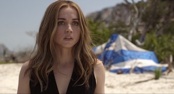 Movie still from “Ghosted” (2023), directed by Dexter Fletcher – A beautiful young woman standing on top of a sandy beach; Close Up shot, Over the shoulder angle