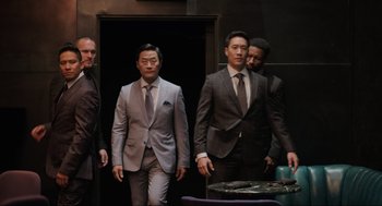 Movie still from “Ghosted” (2023), directed by Dexter Fletcher – A group of men in suits and ties standing next to each other; Medium shot, Over the shoulder angle