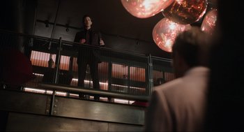 Movie still from “Ghosted” (2023), directed by Dexter Fletcher – A man standing on top of a railing in a room; Wide shot, Low angle