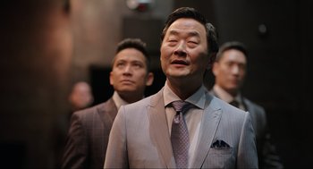 Movie still from “Ghosted” (2023), directed by Dexter Fletcher – A group of men standing next to each other wearing suits and ties; Close Up shot, Over the shoulder angle