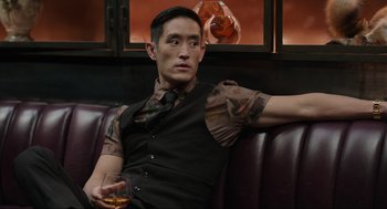 Movie still from “Ghosted” (2023), directed by Dexter Fletcher – A man sitting on a couch holding a glass of wine; Medium shot, Over the shoulder angle