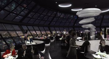 Movie still from “Ghosted” (2023), directed by Dexter Fletcher – People are sitting at tables in a restaurant overlooking a city; Extreme Wide shot, High angle