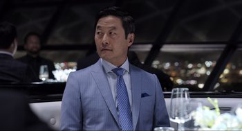Movie still from “Ghosted” (2023), directed by Dexter Fletcher – A man wearing a suit and tie sitting at a table; Close Up shot, Over the shoulder angle
