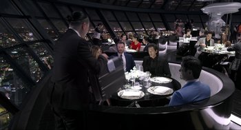 Movie still from “Ghosted” (2023), directed by Dexter Fletcher – A group of people sitting at a table with plates and silverware on it; Wide shot, High angle