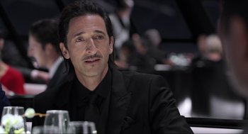 Movie still from “Ghosted” (2023), directed by Dexter Fletcher – A man in a black suit sitting at a table; Close Up shot, Over the shoulder angle