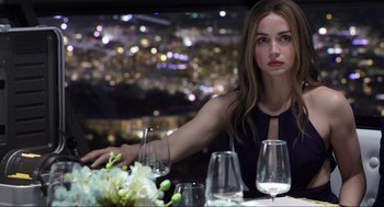 Movie still from “Ghosted” (2023), directed by Dexter Fletcher – A woman sitting at a table with a glass of wine in front of her; Medium shot, Over the shoulder angle