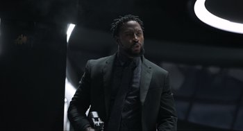 Movie still from “Ghosted” (2023), directed by Dexter Fletcher – A man in a suit and tie holding a gun; Medium shot, Low angle