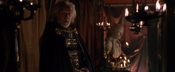 Movie still from “Gladiator” (2000), directed by Ridley Scott – An old man with a long white beard standing next to a statue; Medium shot, Over the shoulder angle