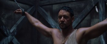 Movie still from “Gladiator” (2000), directed by Ridley Scott – A man with a beard and a necklace is holding his arm up in the air; Close Up shot, Low angle