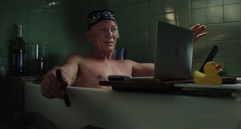 Movie still from “Glass Onion” (2022), directed by Rian Johnson – An older man sitting in a bath tub next to a lap top computer; Medium shot, High angle