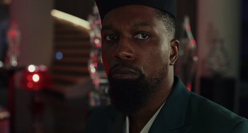 Movie still from “Glass Onion” (2022), directed by Rian Johnson – A person wearing a suit and a hat; Close Up shot, Low angle