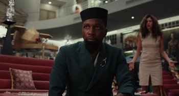 Movie still from “Glass Onion” (2022), directed by Rian Johnson – A man with a beard wearing a green suit and a hat; Medium shot, Low angle